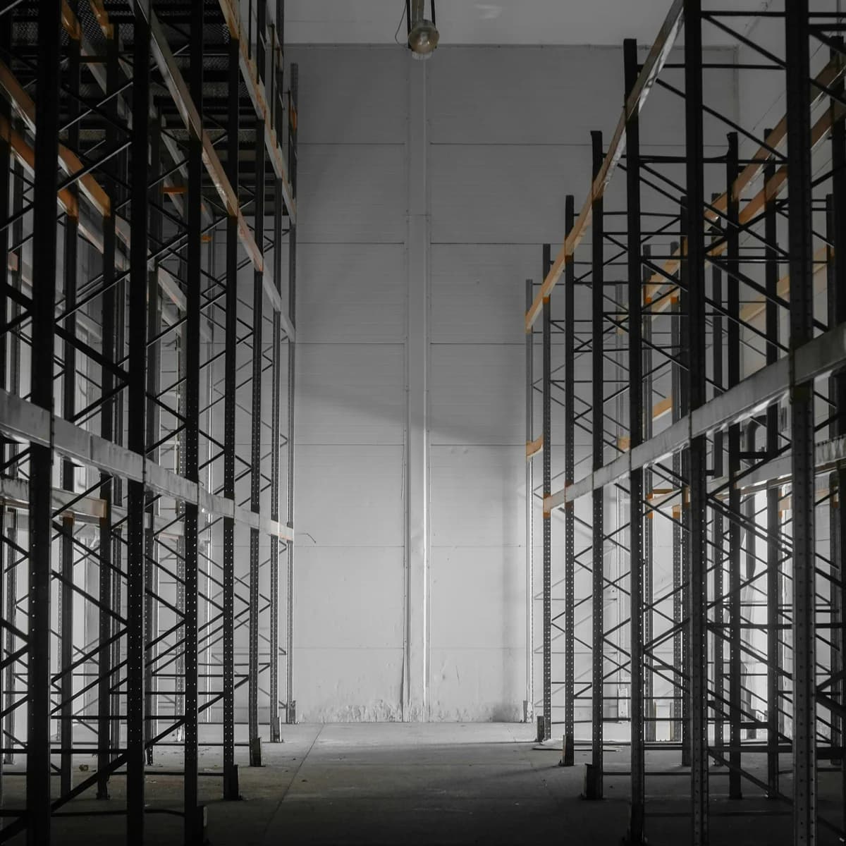 Hoher Gang zwischen leeren Palettenregalen in einer Lagerhalle, der auf eine helle Rückwand zuläuft